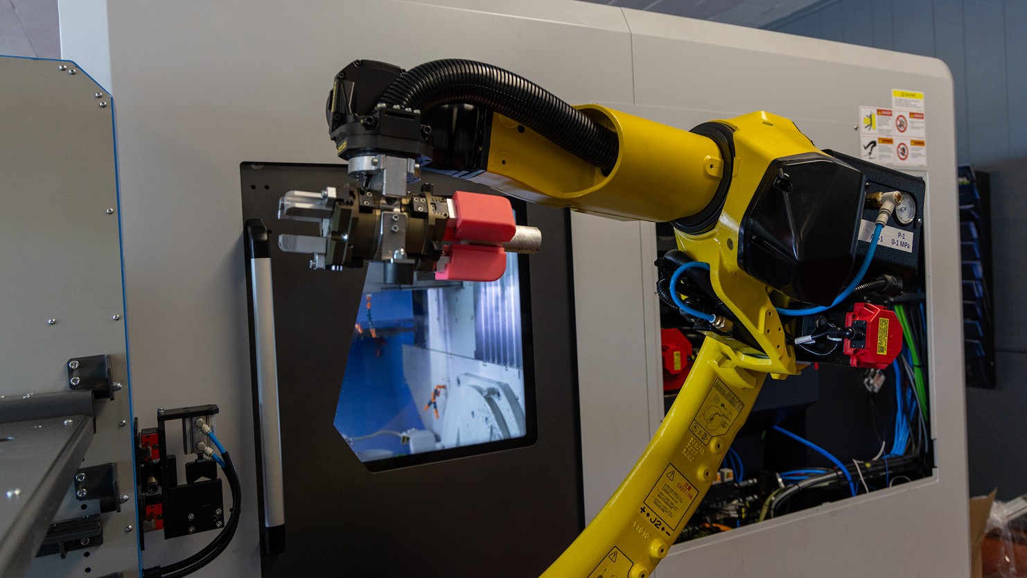 Yellow industrial robot with gripper positioned at a CNC machine